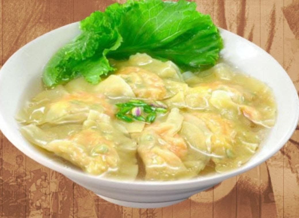 A close-up of a bowl of savory dumplings or wontons in broth, garnished with fresh lettuce.