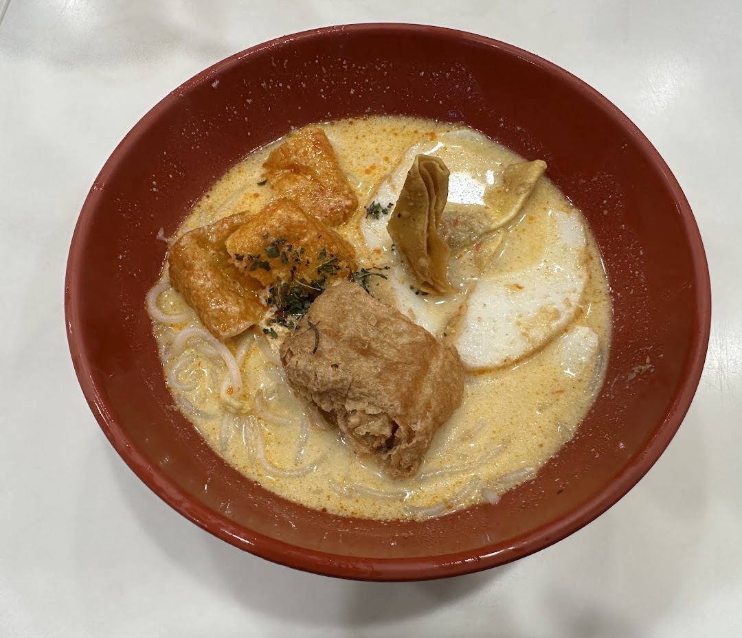 A close-up of a delicious bowl of creamy noodle soup with various toppings in a red bowl.