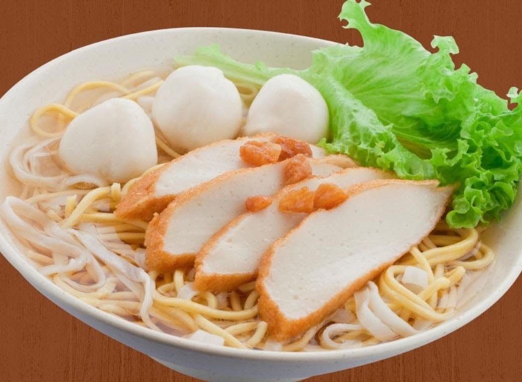 A close-up of a bowl of noodles with fish cakes, fish balls, and fresh lettuce.