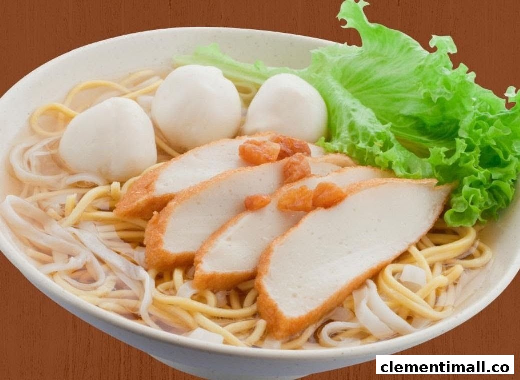 A close-up of a bowl of noodles with fish cakes, fish balls, and fresh lettuce.