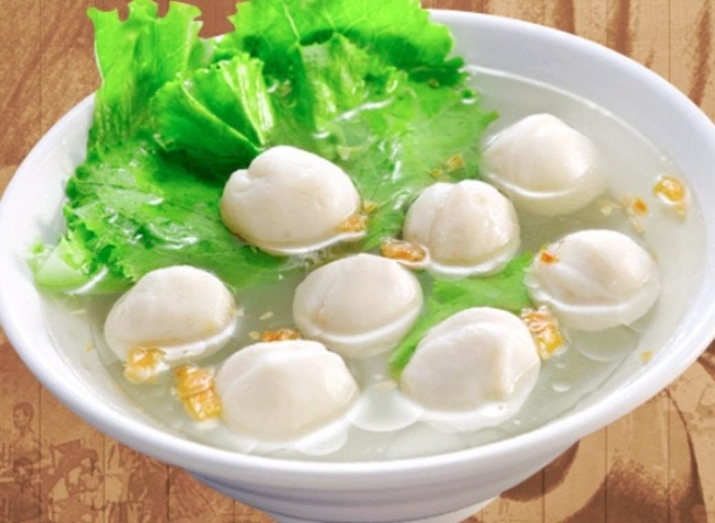 A white bowl filled with clear broth, several white fish balls, and fresh green lettuce.
