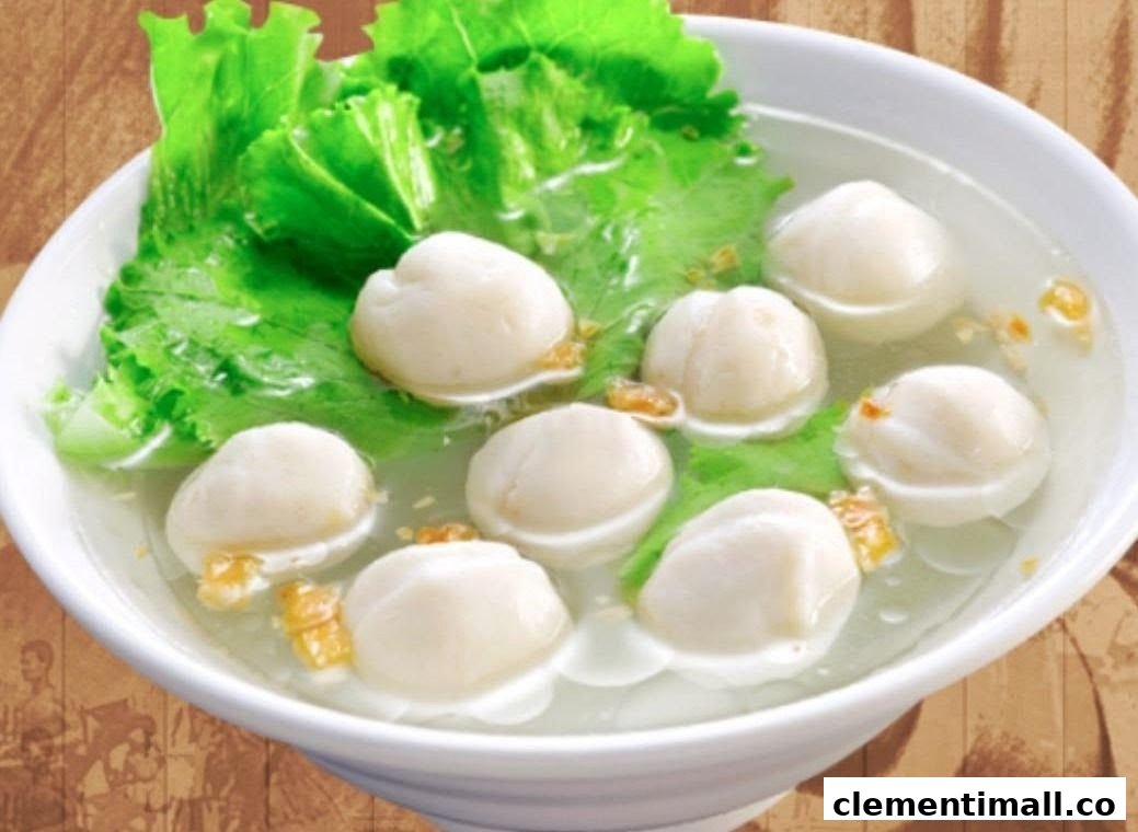 A white bowl filled with clear broth, several white fish balls, and fresh green lettuce.
