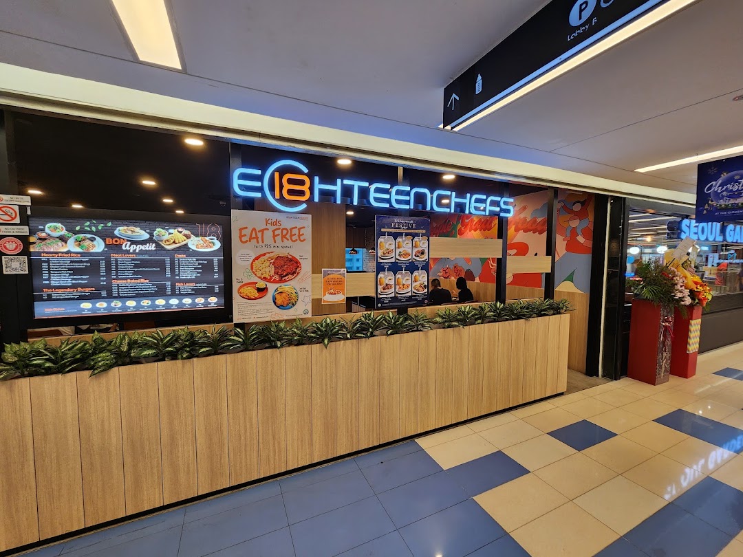 The brightly lit entrance of Eighteen Chefs restaurant with a digital menu board and promotional posters.