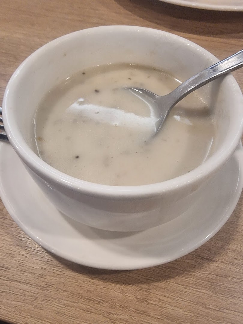 A white bowl of creamy mushroom soup with a spoon on a wooden table.