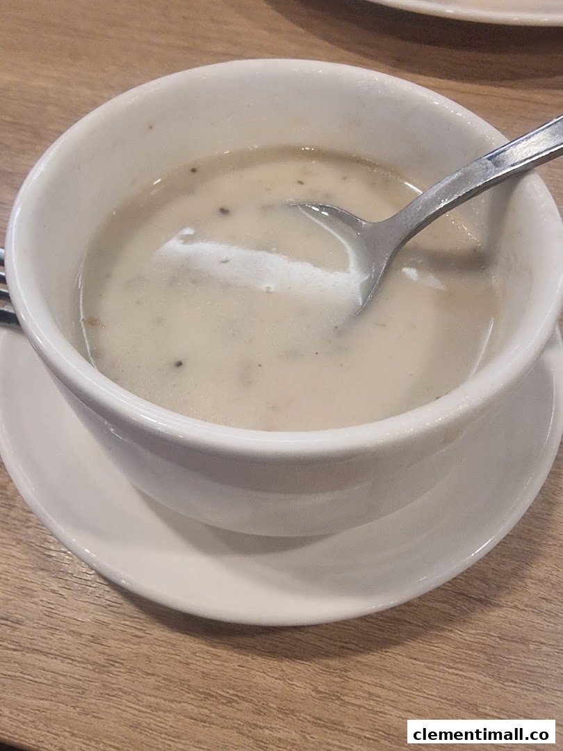 A white bowl of creamy mushroom soup with a spoon on a wooden table.