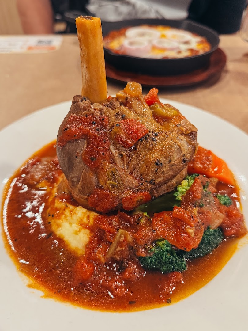 A close-up of a delicious lamb shank served with mashed potatoes, vegetables, and rich tomato sauce.