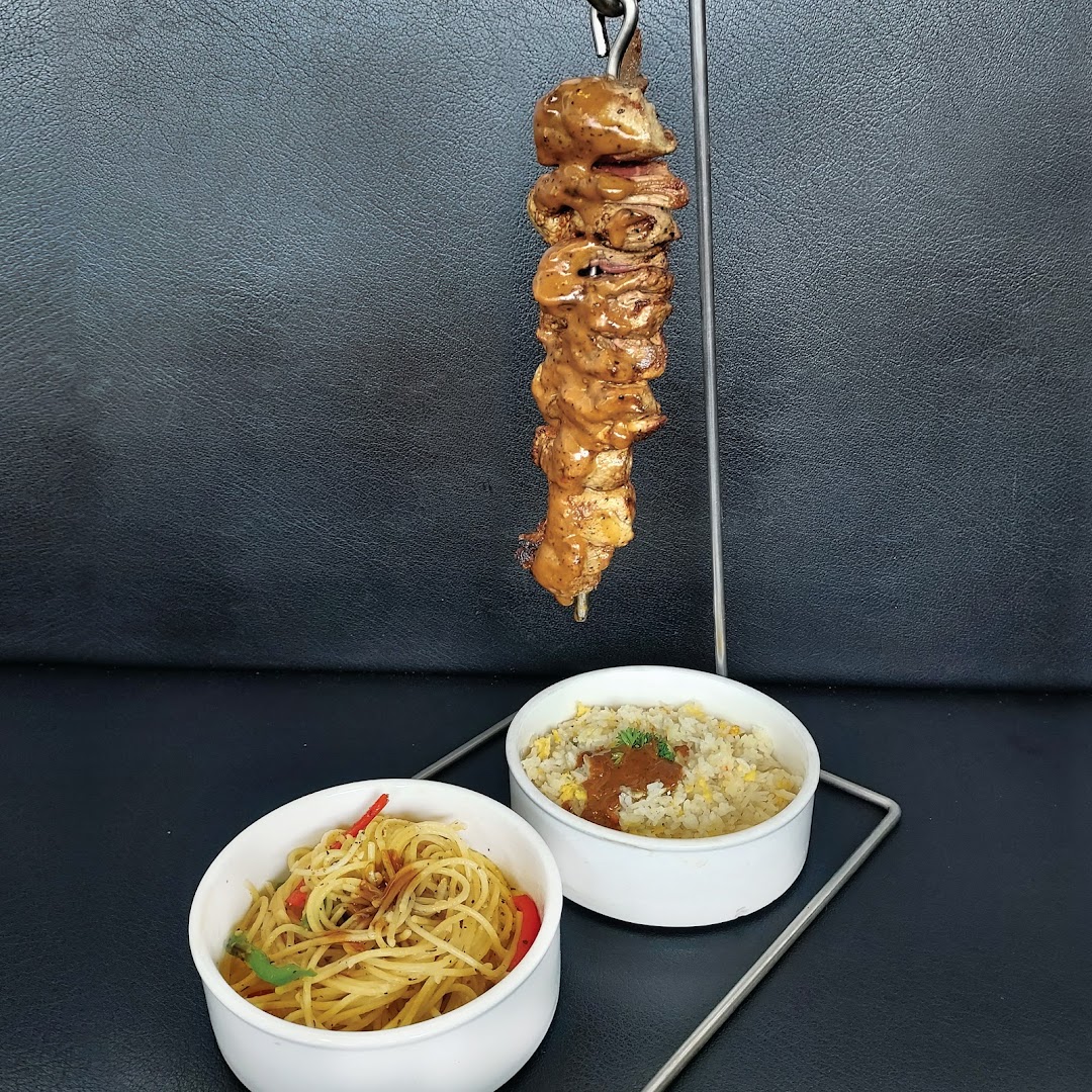 A delicious skewer of meat served with a side of spaghetti and fried rice.