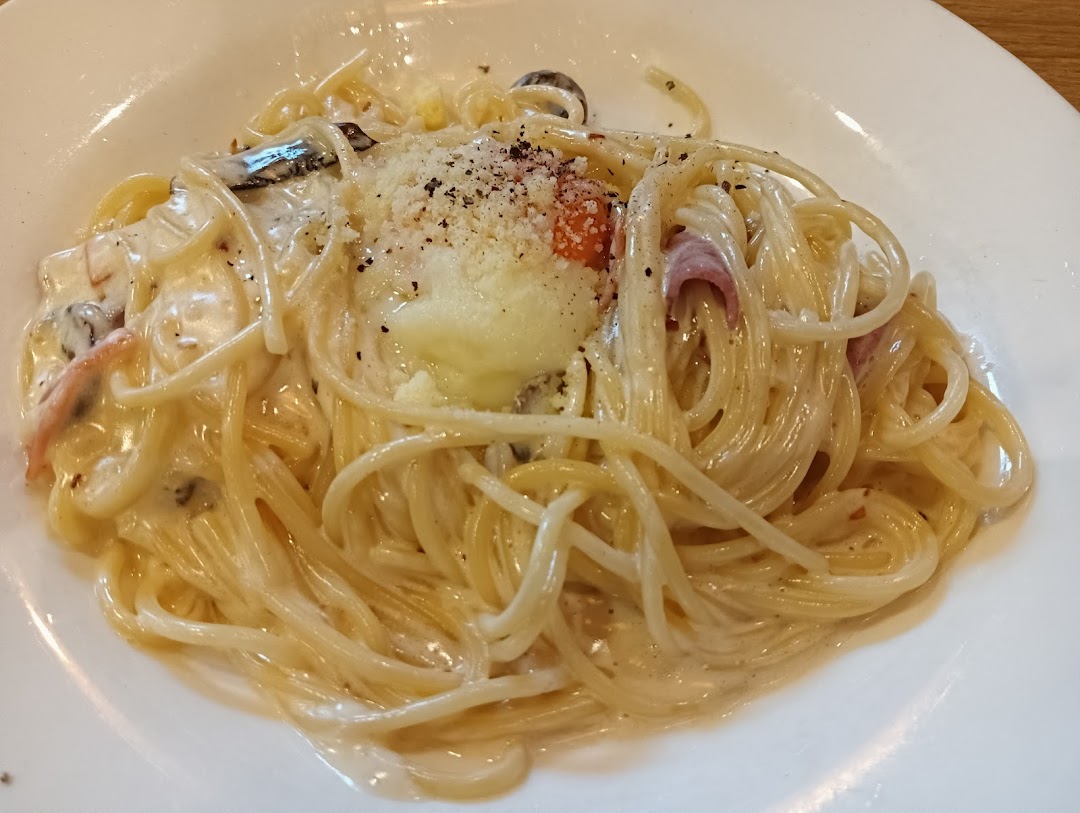 A close-up of a creamy pasta dish with a poached egg, bacon, and mushrooms on a white plate.