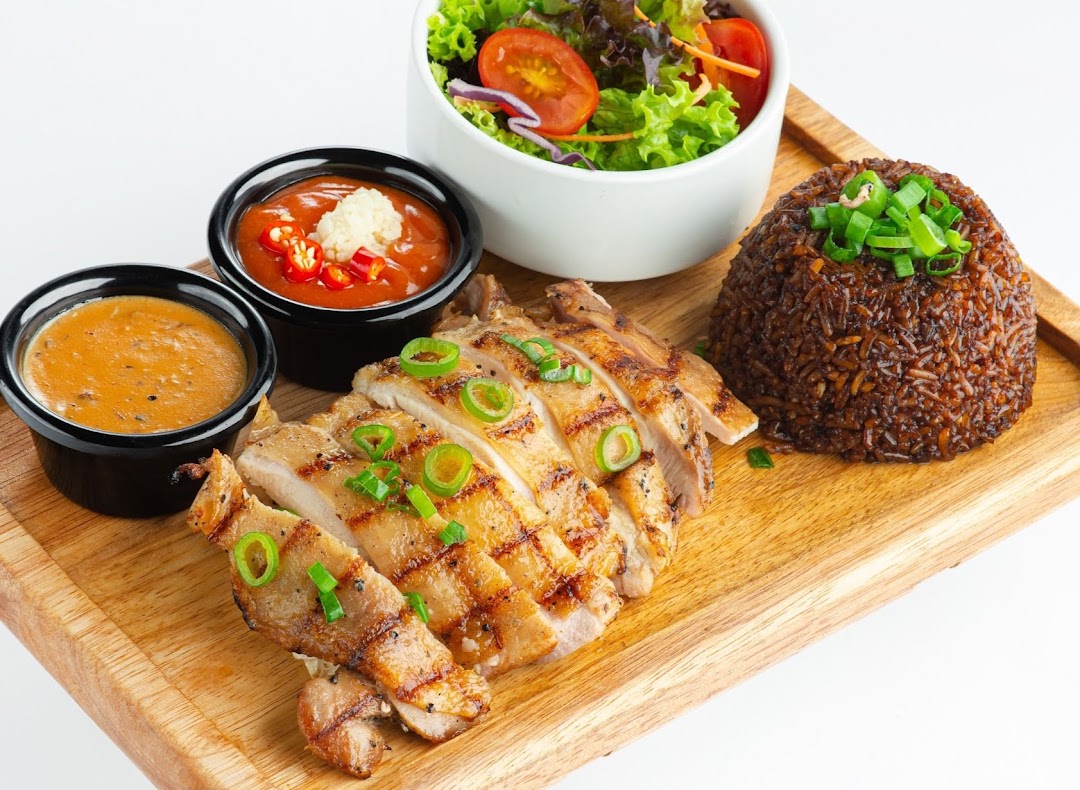 A grilled chicken dish with rice, salad, and two sauces served on a wooden board.
