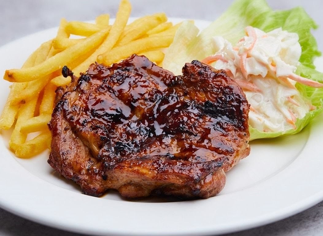 A delicious glazed chicken chop served with golden fries and fresh coleslaw on a white plate.