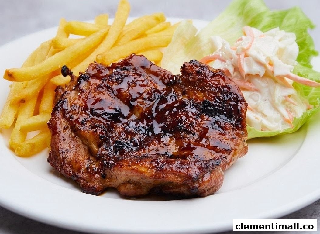 A delicious glazed chicken chop served with golden fries and fresh coleslaw on a white plate.