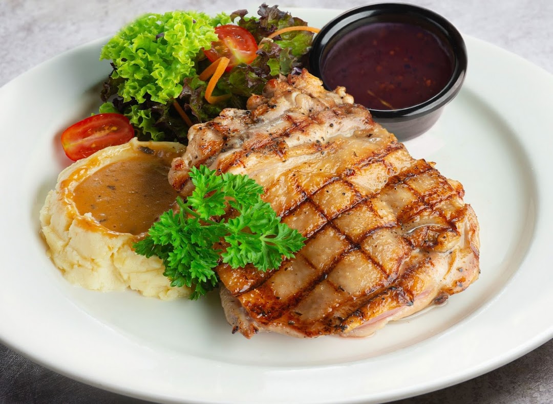 A grilled chicken steak served with mashed potatoes, fresh salad, and a side of sauce.