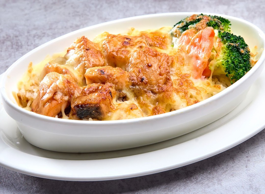 A baked dish featuring cheesy salmon chunks, rice, broccoli, and carrots in a white oval bowl.