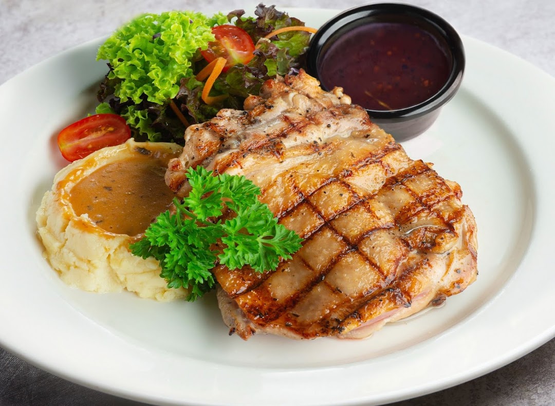 A perfectly grilled chicken chop served with creamy mashed potatoes, fresh salad, and a rich sauce.