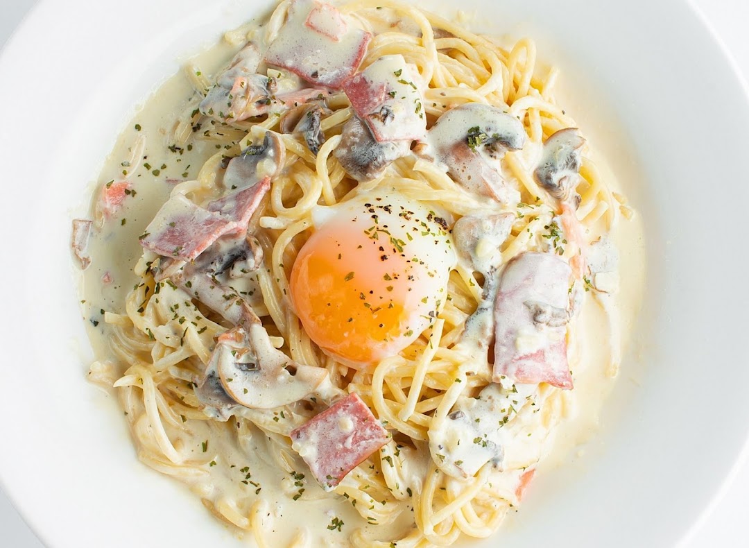 A creamy spaghetti carbonara dish with bacon, mushrooms, and a perfectly poached egg.