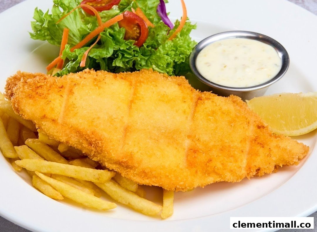 A plate of golden-fried fish and chips with a side salad, lemon wedge, and tartar sauce.