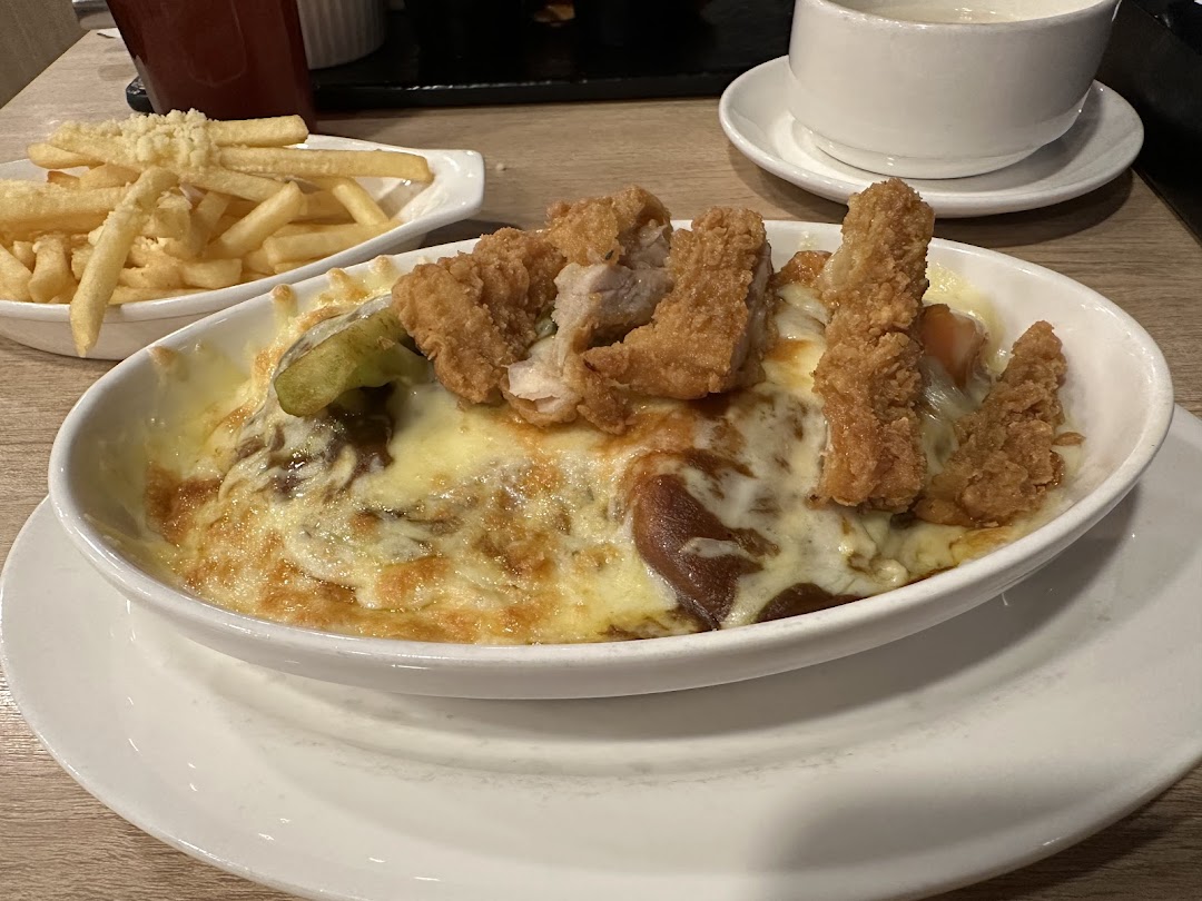 A close-up of a cheesy baked rice dish topped with crispy fried chicken and a side of golden fries.