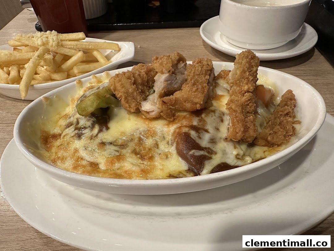 A close-up of a cheesy baked rice dish topped with crispy fried chicken and a side of golden fries.