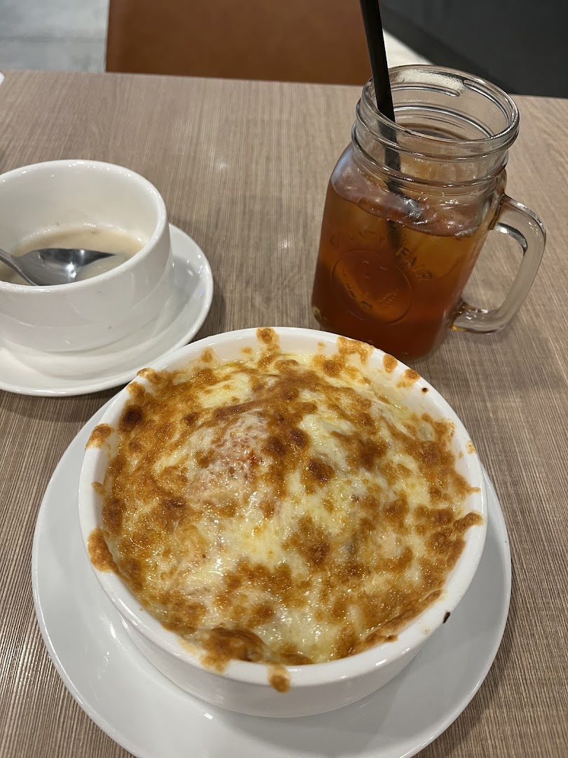 A close-up of a cheesy baked dish, soup, and iced tea on a wooden table.