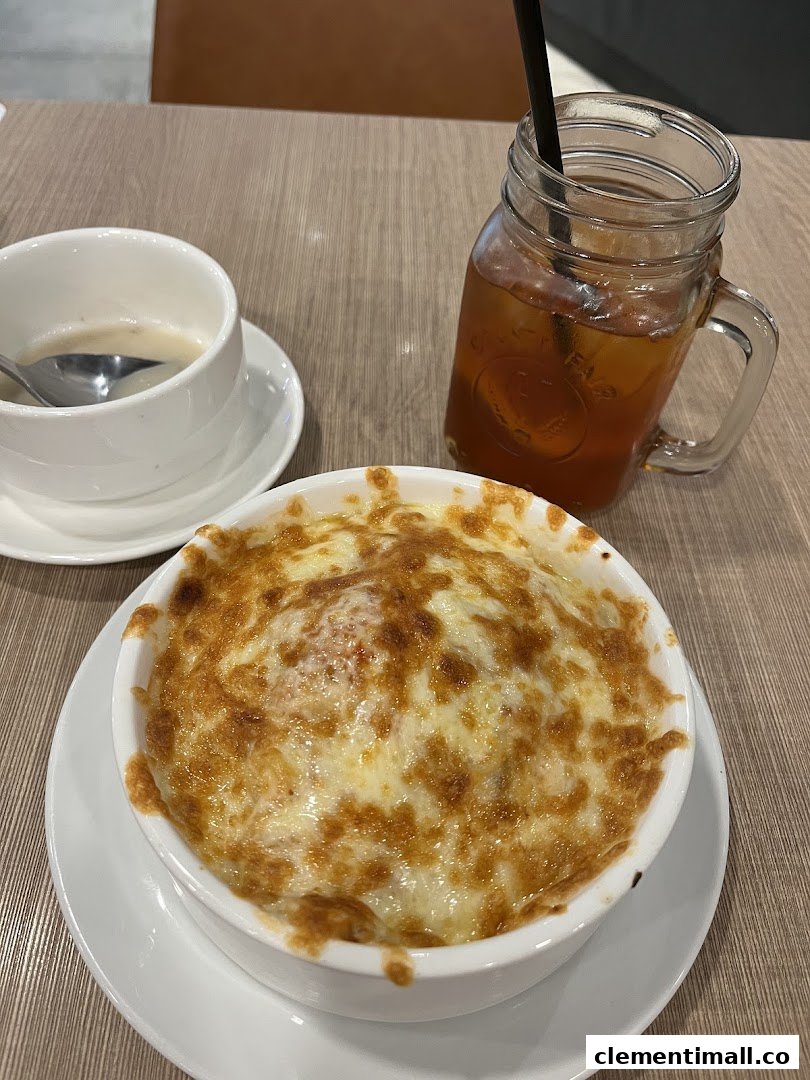 A close-up of a cheesy baked dish, soup, and iced tea on a wooden table.