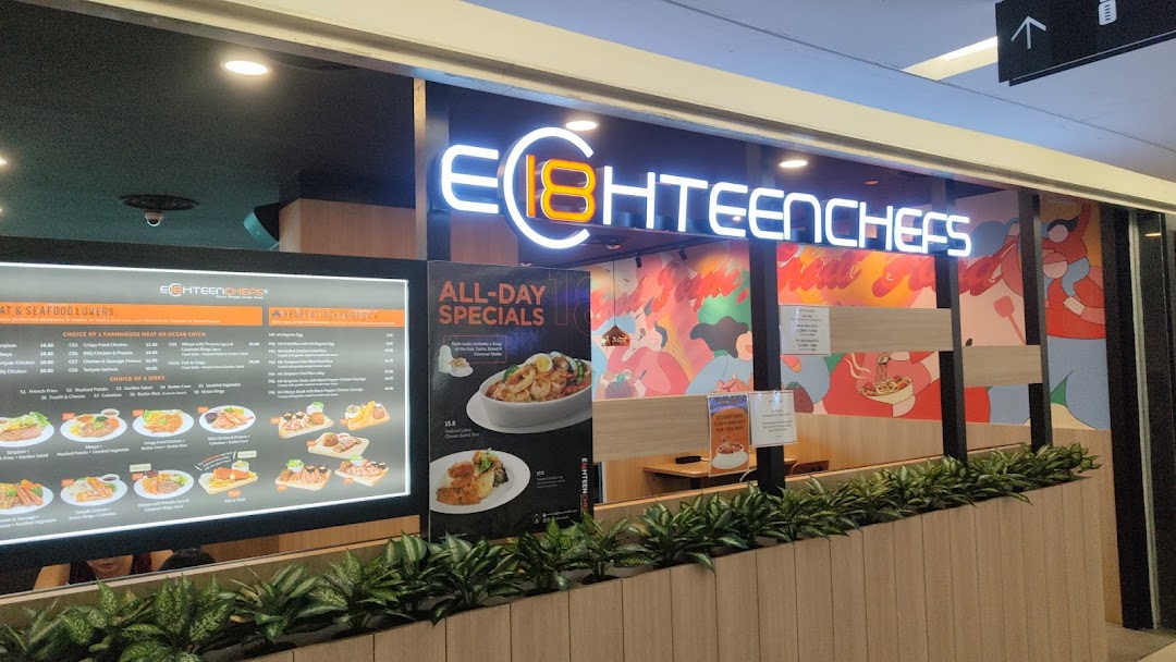 The brightly lit exterior of Eighteen Chefs restaurant, featuring its logo, menu displays, and colorful wall art.