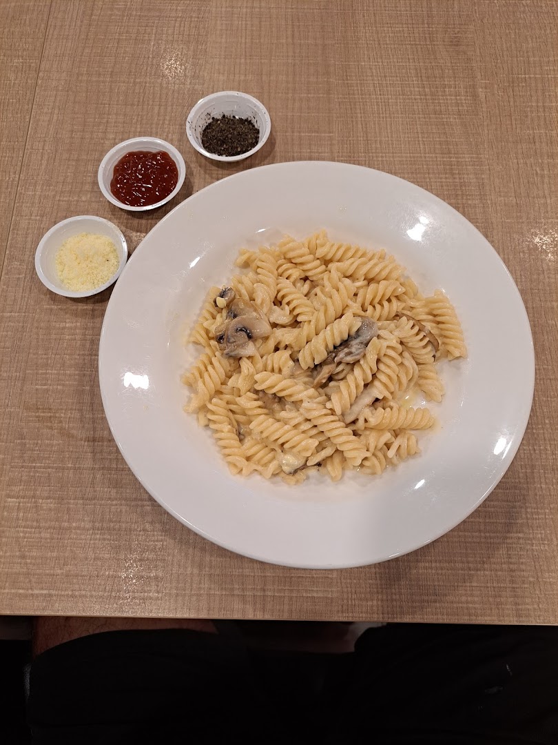 A creamy mushroom fusilli pasta dish served with parmesan, chili flakes, and ketchup.