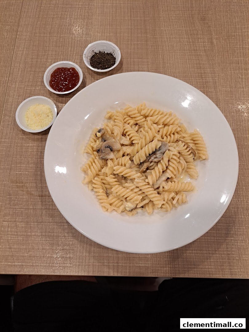 A creamy mushroom fusilli pasta dish served with parmesan, chili flakes, and ketchup.