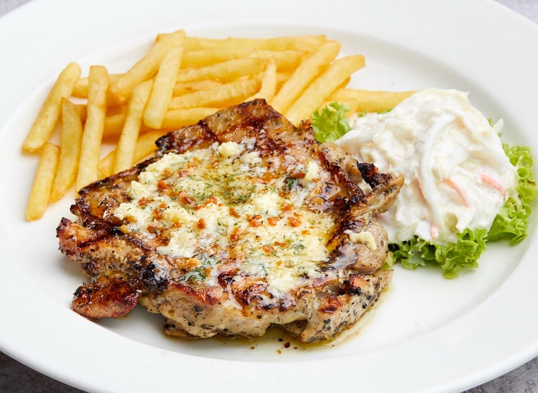 A grilled chicken chop topped with cheese and herbs, served with fries and coleslaw on a white plate.