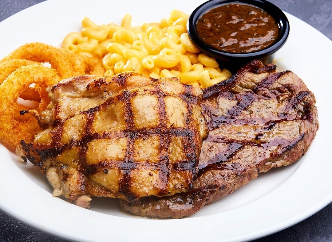 A delicious plate featuring grilled chicken, steak, mac & cheese, onion rings, and sauce.