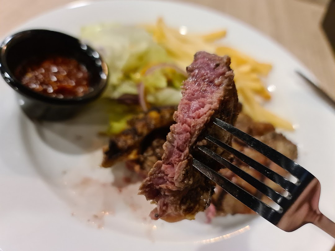 A close-up of a perfectly cooked steak on a fork, served with fries and salad.