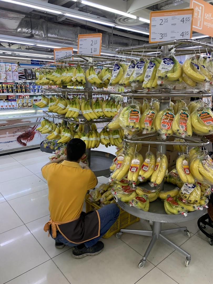A supermarket staff member organizes fresh bananas on a display stand at FairPrice Finest.