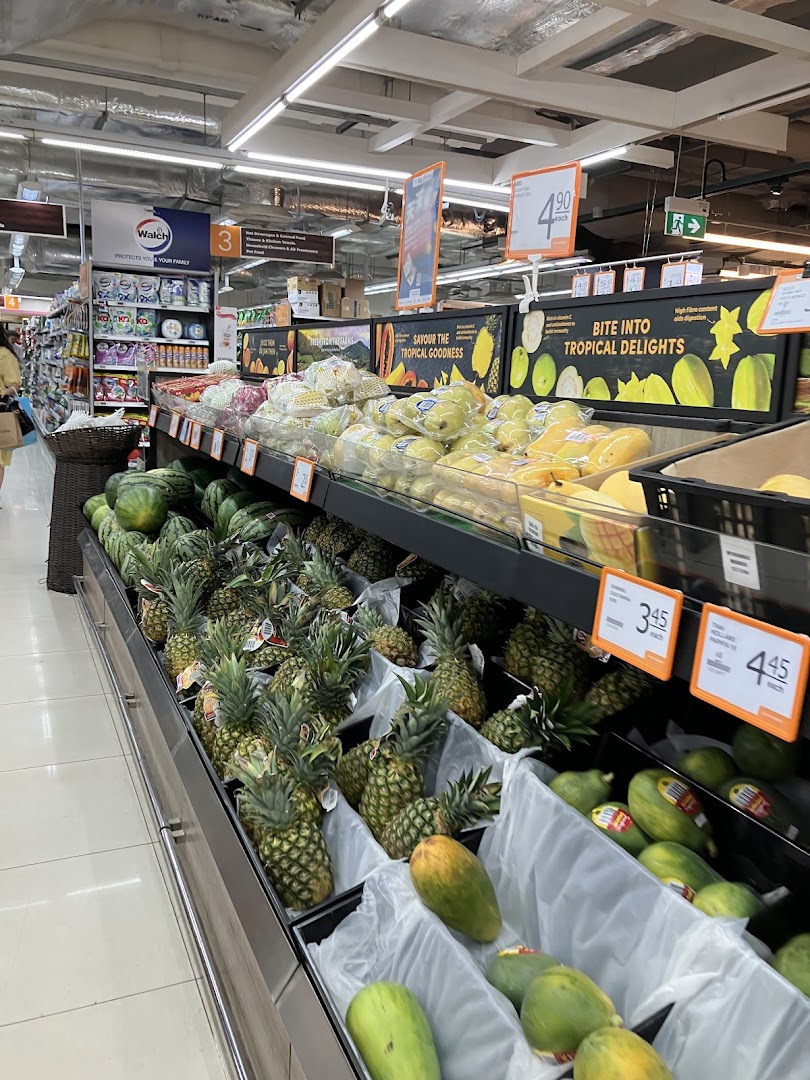 An aisle at FairPrice Finest showcasing a vibrant display of fresh tropical fruits like pineapples, watermelons, and papayas.