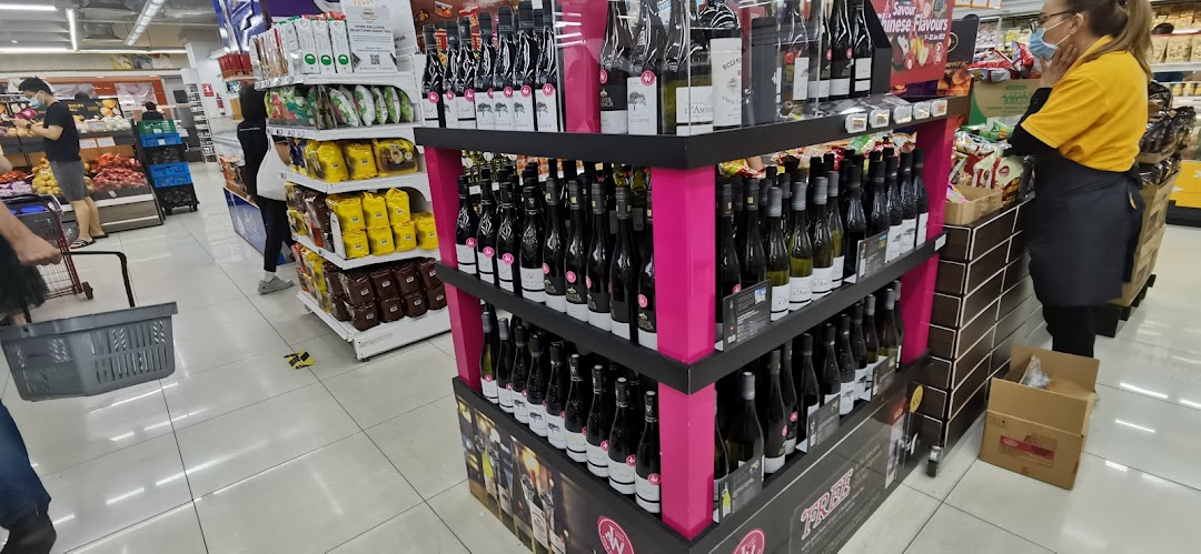 An interior view of FairPrice Finest, showcasing a prominent wine display, fresh produce, and shoppers.