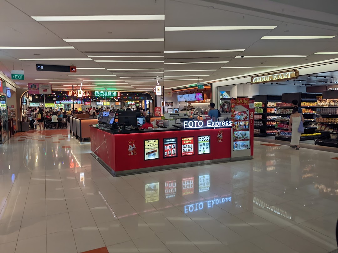 A Foto Express kiosk offering photo services, including digitizing films and passport photos, located in a bustling mall.