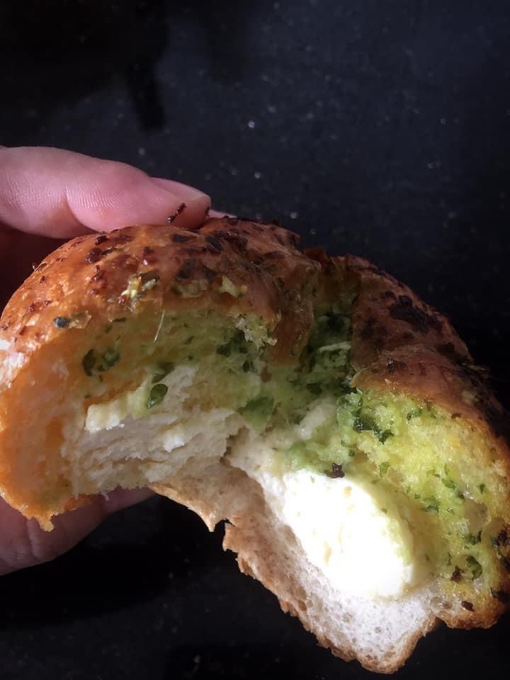 A hand holds a bitten savory bun, revealing a creamy white and green herb filling.