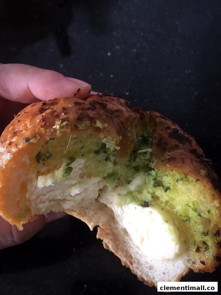 A hand holds a bitten savory bun, revealing a creamy white and green herb filling.