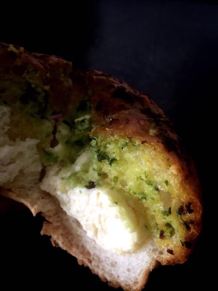 A close-up of a savory bread with a creamy filling and green herbs, showing a bite taken.