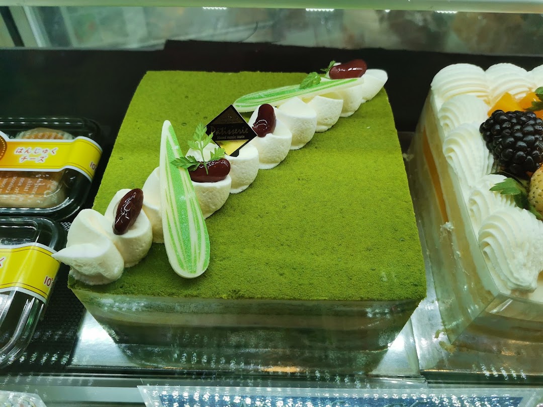 A vibrant green matcha cake with elegant cream decorations displayed alongside other delicious pastries.