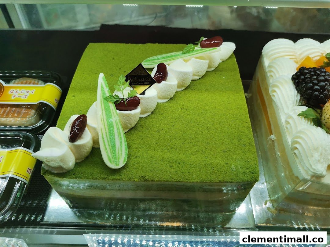 A vibrant green matcha cake with elegant cream decorations displayed alongside other delicious pastries.