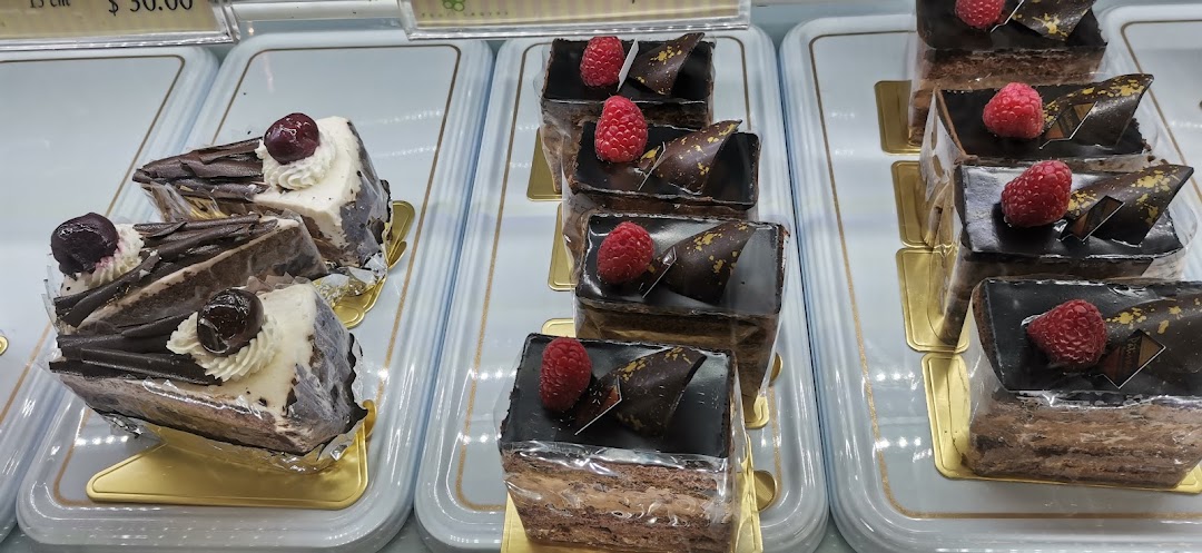 A vibrant display of chocolate and cream cakes, some topped with raspberries and cherries.