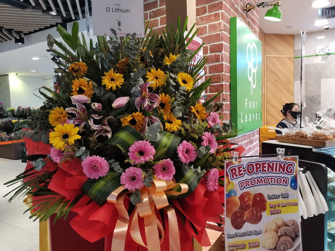 A vibrant floral arrangement and re-opening promotion sign at the Four Leaves bakery counter.