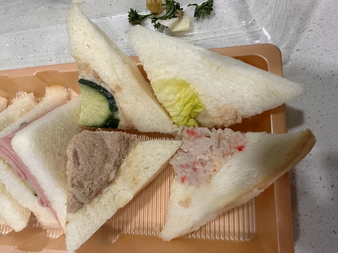 A close-up of assorted finger sandwiches, including ham, tuna, cucumber, and crab stick, in a plastic tray.