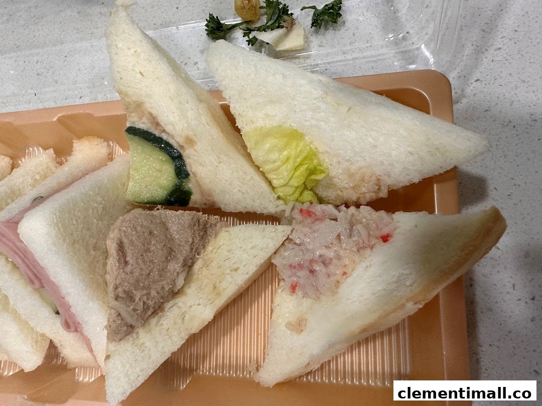 A close-up of assorted finger sandwiches, including ham, tuna, cucumber, and crab stick, in a plastic tray.