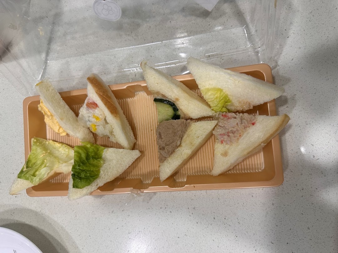 A variety of triangular finger sandwiches with different fillings presented in a clear plastic tray.