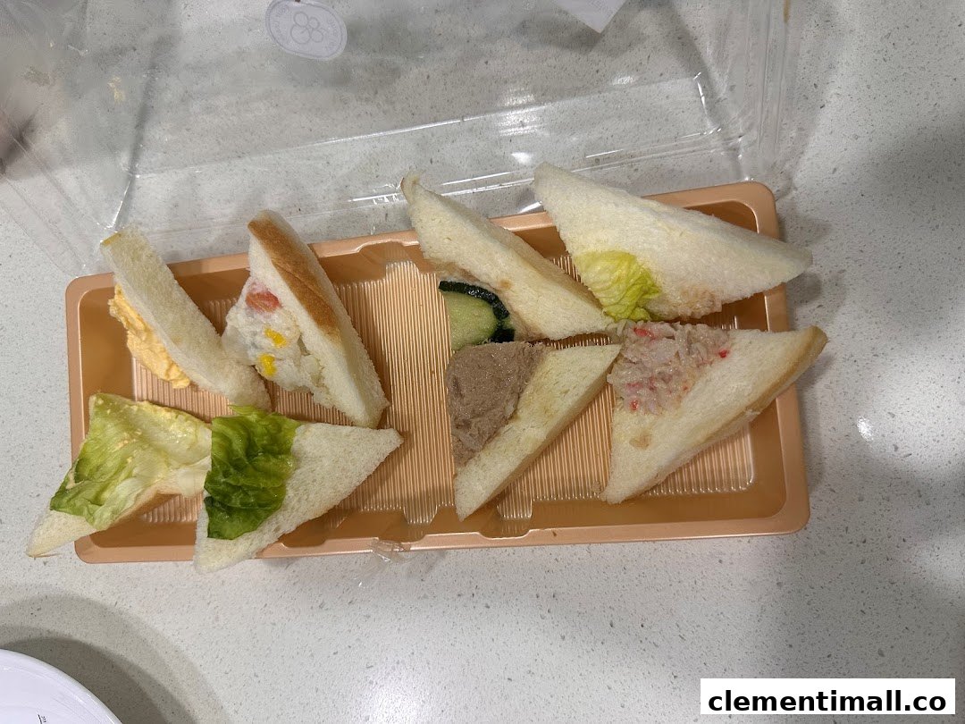 A variety of triangular finger sandwiches with different fillings presented in a clear plastic tray.