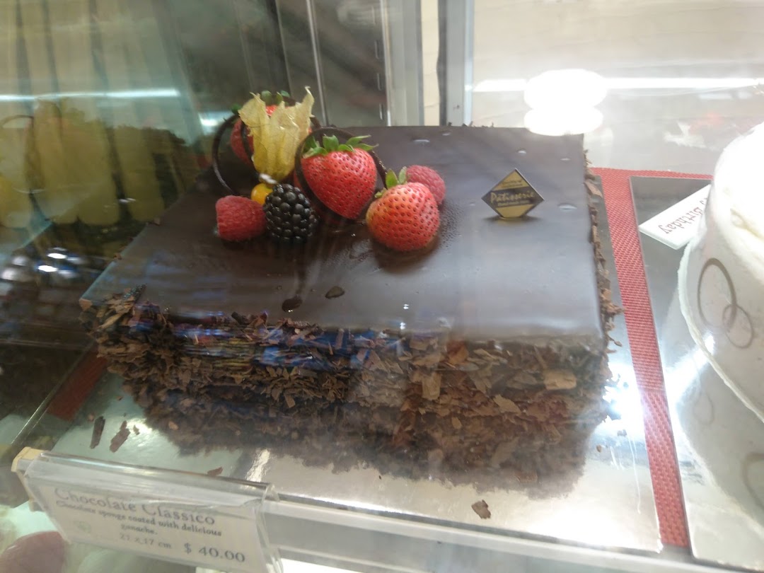 A decadent chocolate cake adorned with fresh berries displayed in a glass case.