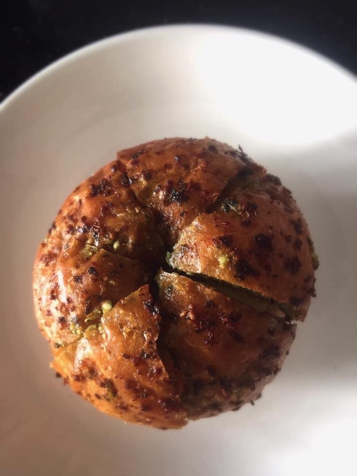 A close-up of a golden-brown, savory bread or bun, possibly garlic bread, served in a white bowl.