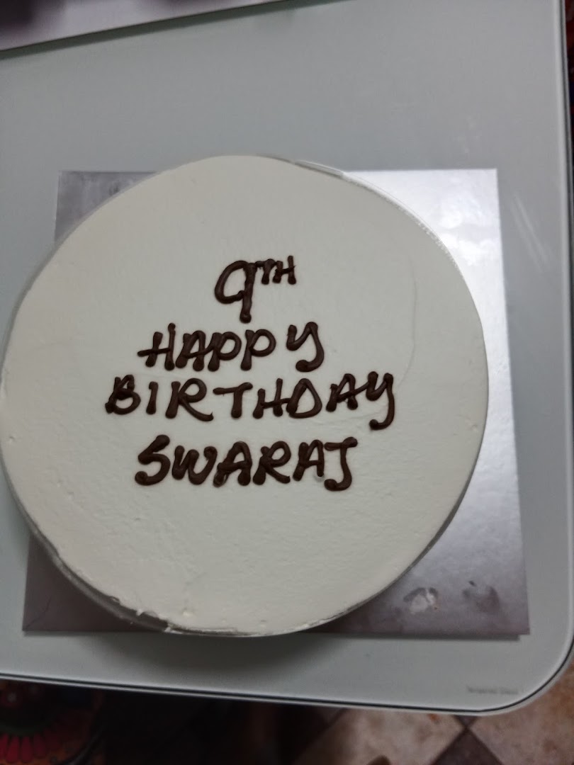 A white birthday cake with chocolate frosting spelling '9th Happy Birthday Swaraj'.