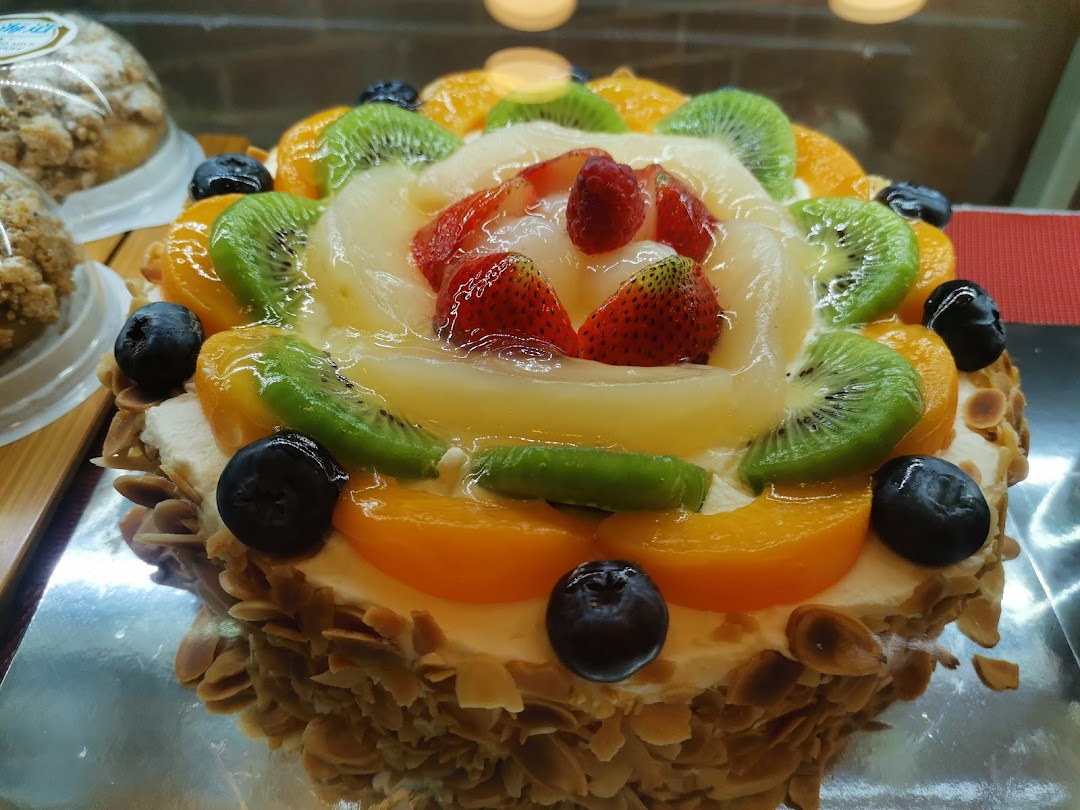 A vibrant fruit cake topped with strawberries, kiwi, peaches, and blueberries, displayed in a bakery.