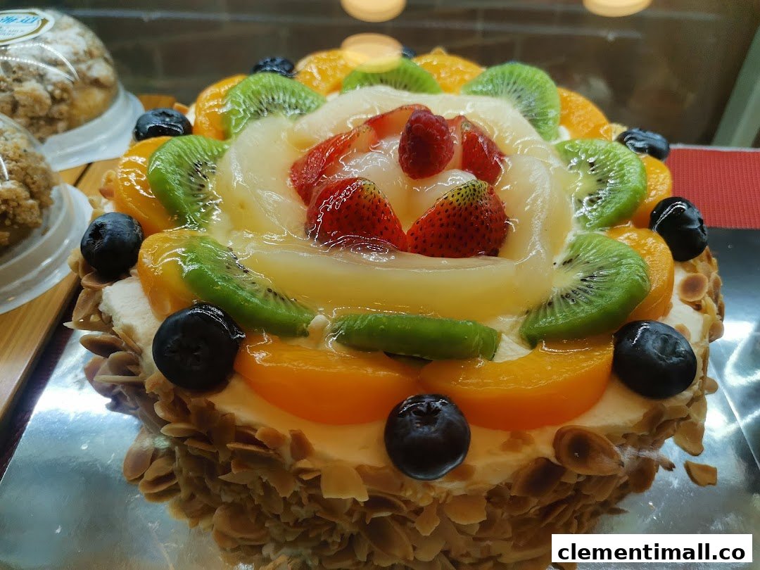 A vibrant fruit cake topped with strawberries, kiwi, peaches, and blueberries, displayed in a bakery.
